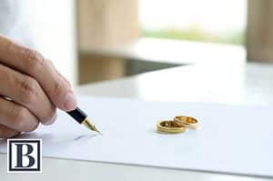 Man signing divorce settlement agreement next to two wedding rings on a table