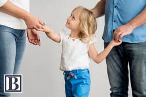 Child holding hands with both parents, reflecting a healthy co-parenting relationship free of parental alienation